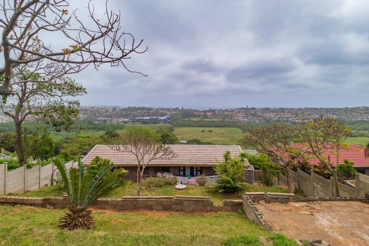 Rear view of the property featuring a tiled roof, concrete boundary walls, and a sloped garden area overlooking the surrounding neighborhood.