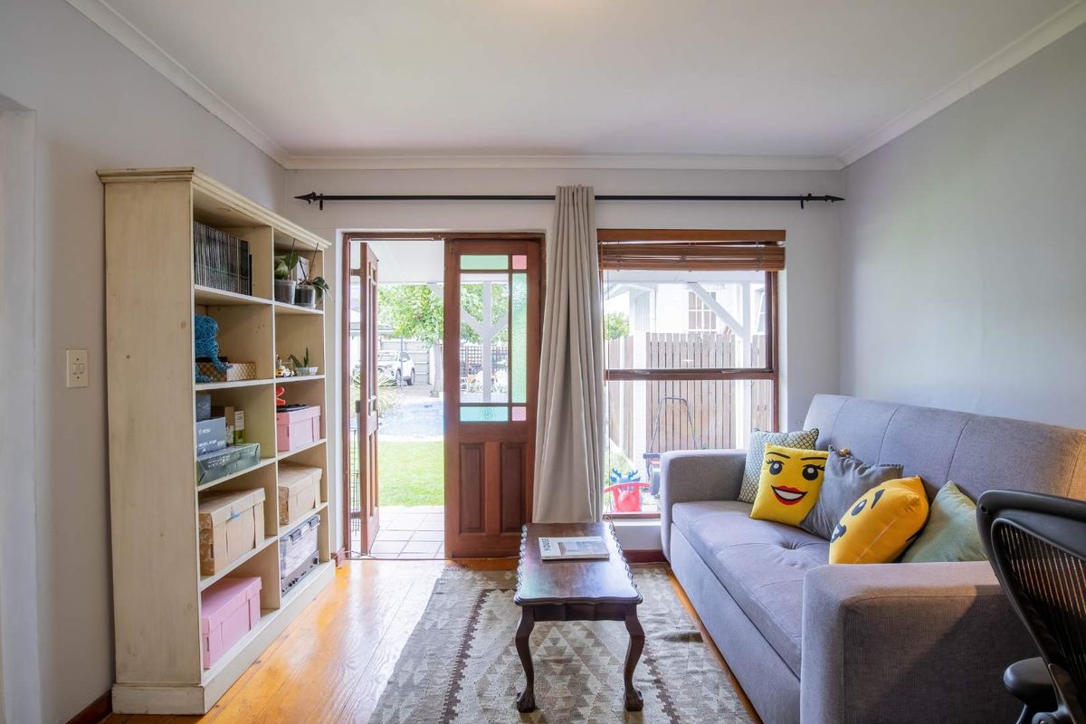 A cozy living room featuring polished timber flooring, a timber-framed door with stained glass accents, and direct access to the rear garden area.