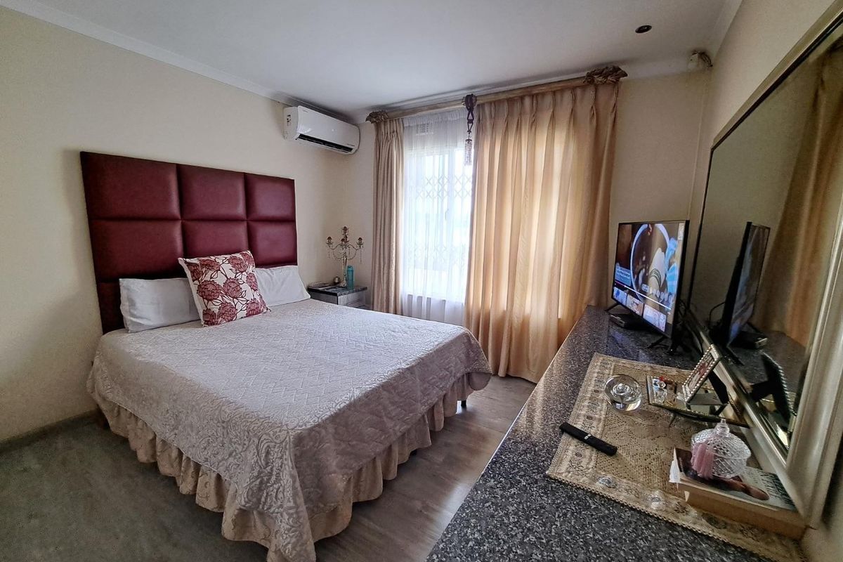 A bedroom featuring laminate flooring, a wall-mounted air conditioning unit, and a built-in granite vanity surface with an integrated mirror.