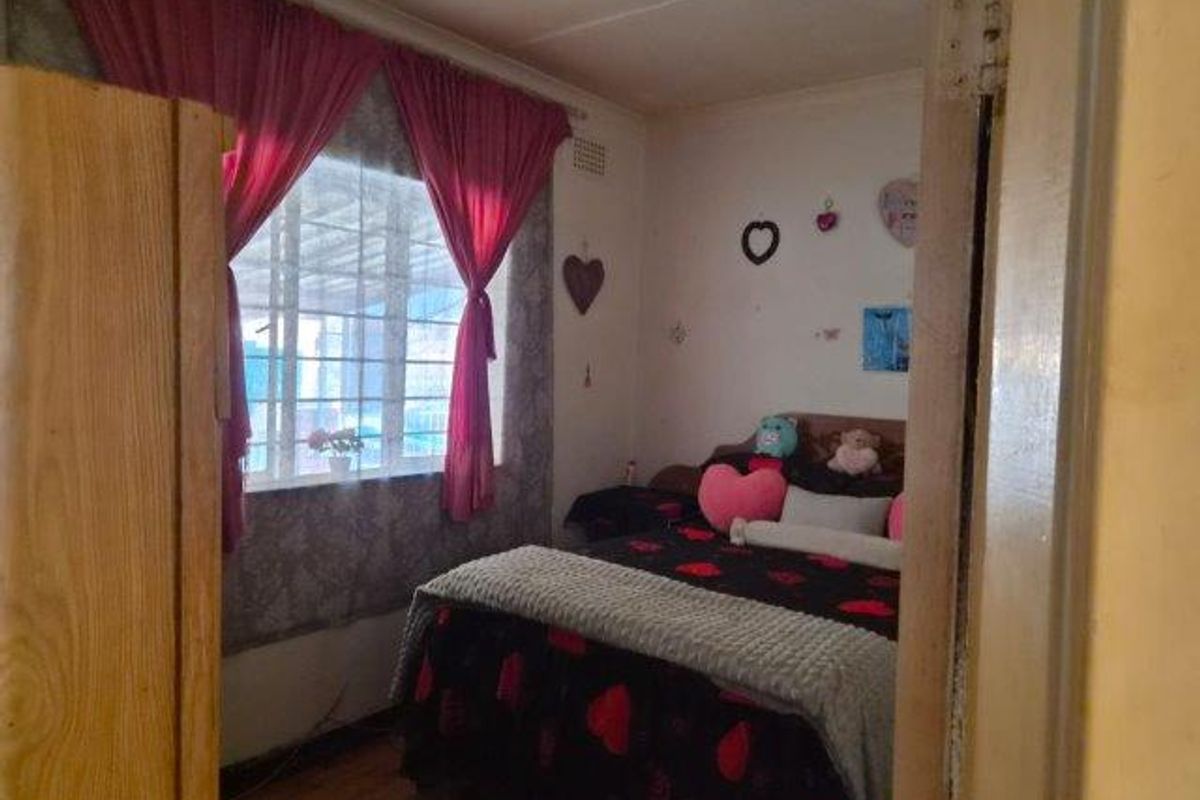 A bedroom featuring timber flooring and a window fitted with security bars.