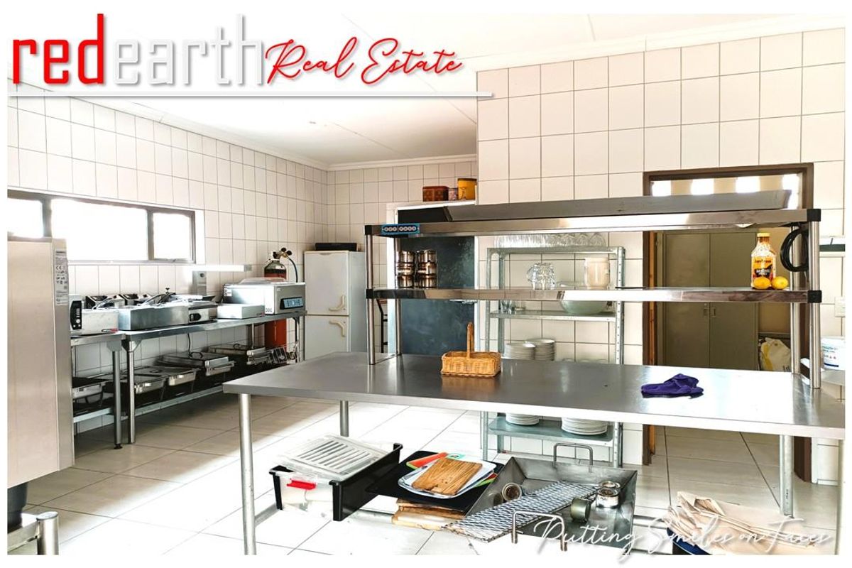 Commercial-style kitchen featuring tiled walls, stainless steel prep tables, and industrial shelving, suitable for high-volume food preparation and catering operations.