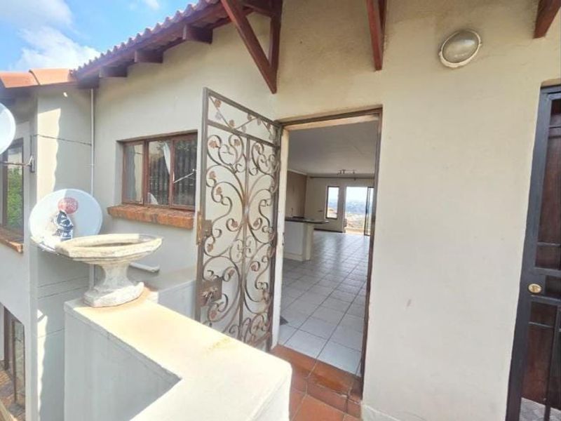Entrance area featuring a decorative wrought iron security gate, tiled patio flooring, and exposed timber roof rafters leading into the main living space.