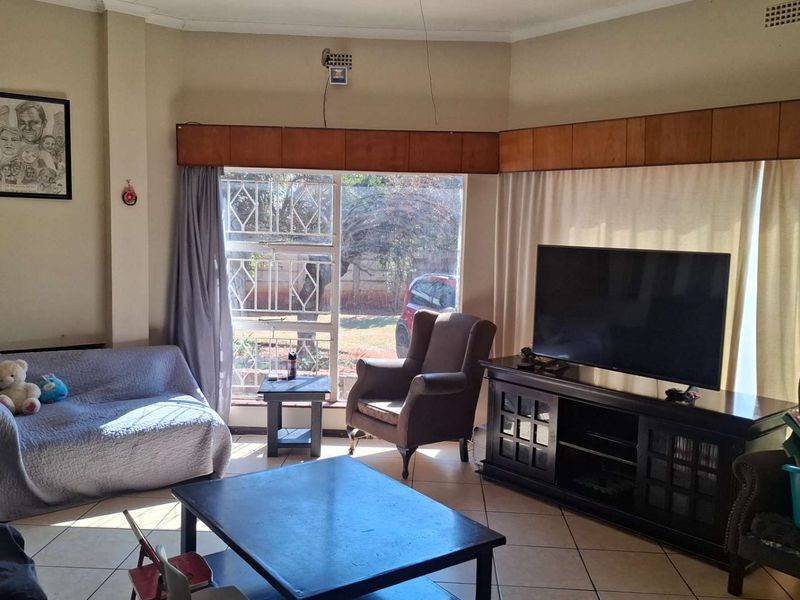 A living room featuring tiled flooring, a large window with security gate, and built-in wooden pelmet detailing.