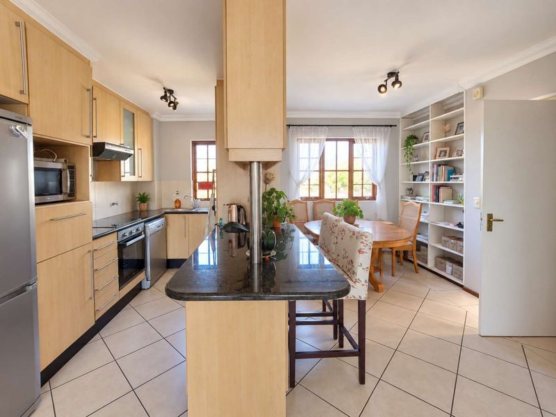 Open-plan kitchen and dining area featuring light wood cabinetry, granite countertops, built-in shelving, and tiled flooring throughout.