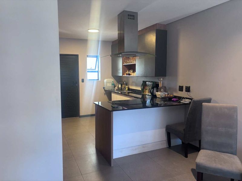 Modern kitchen featuring dark cabinetry, granite countertops, and a stainless steel extractor fan, complemented by neutral tiled flooring.