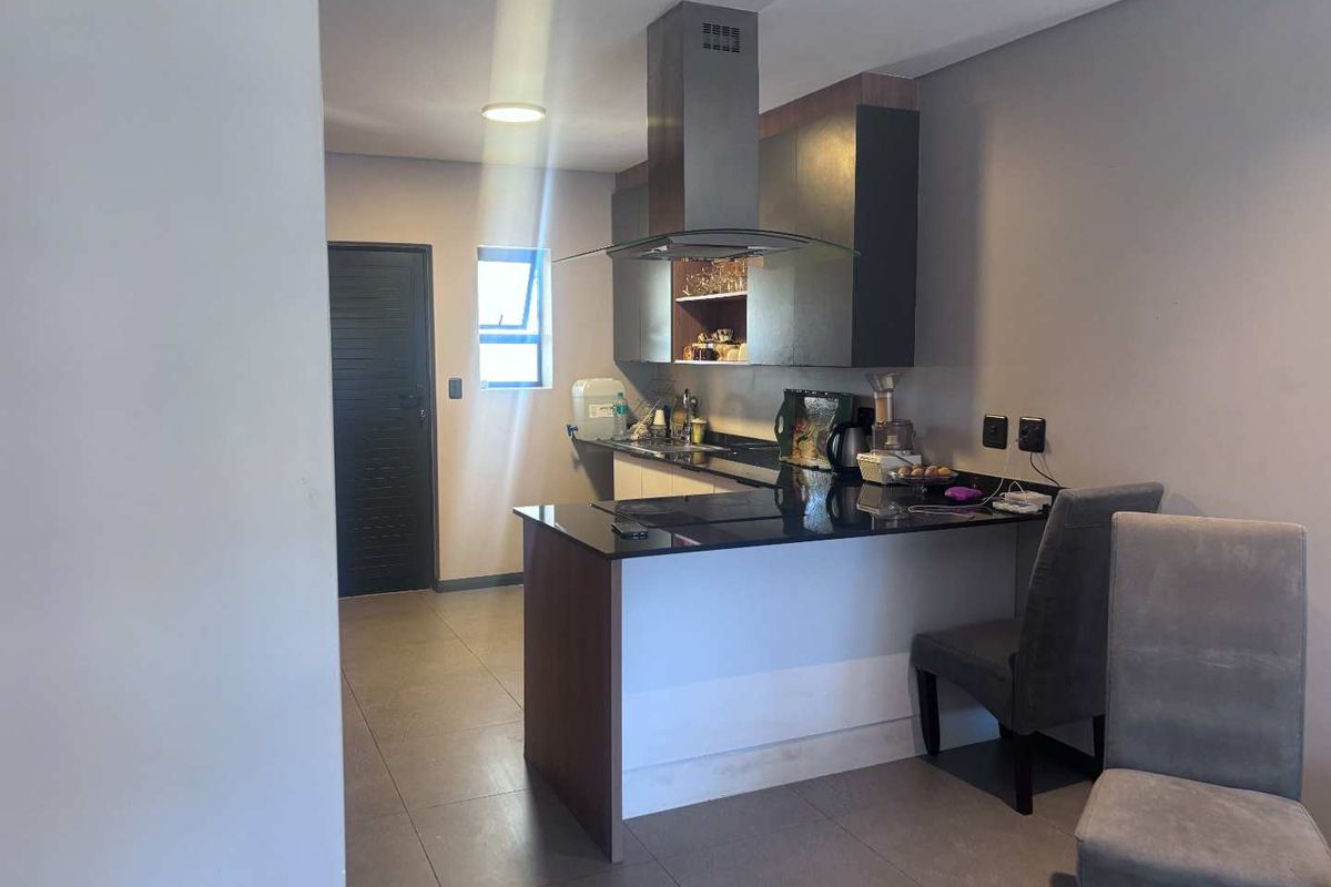 Modern kitchen featuring dark cabinetry, granite countertops, and a stainless steel extractor fan, complemented by neutral tiled flooring.
