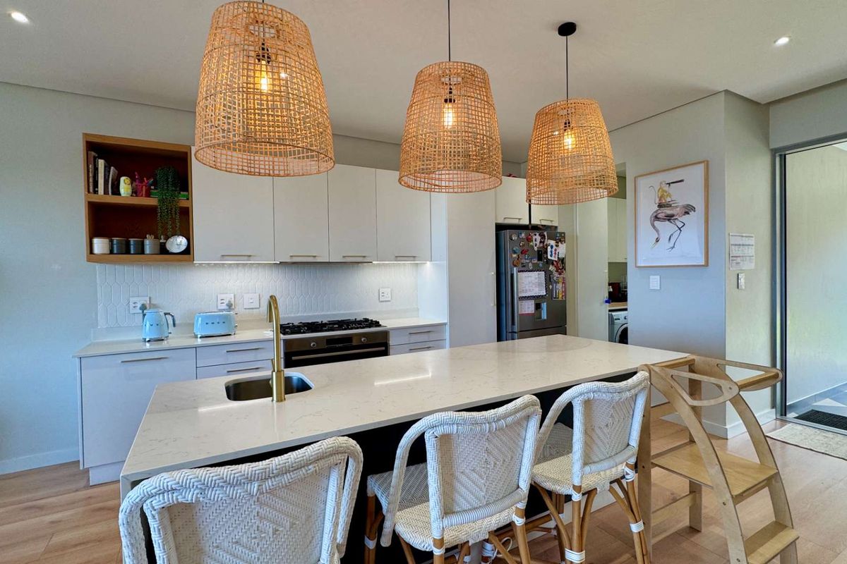 Modern kitchen featuring a central island with quartz countertops, brass fixtures, built-in appliances, and stylish pendant lighting, seamlessly connected to the living area.