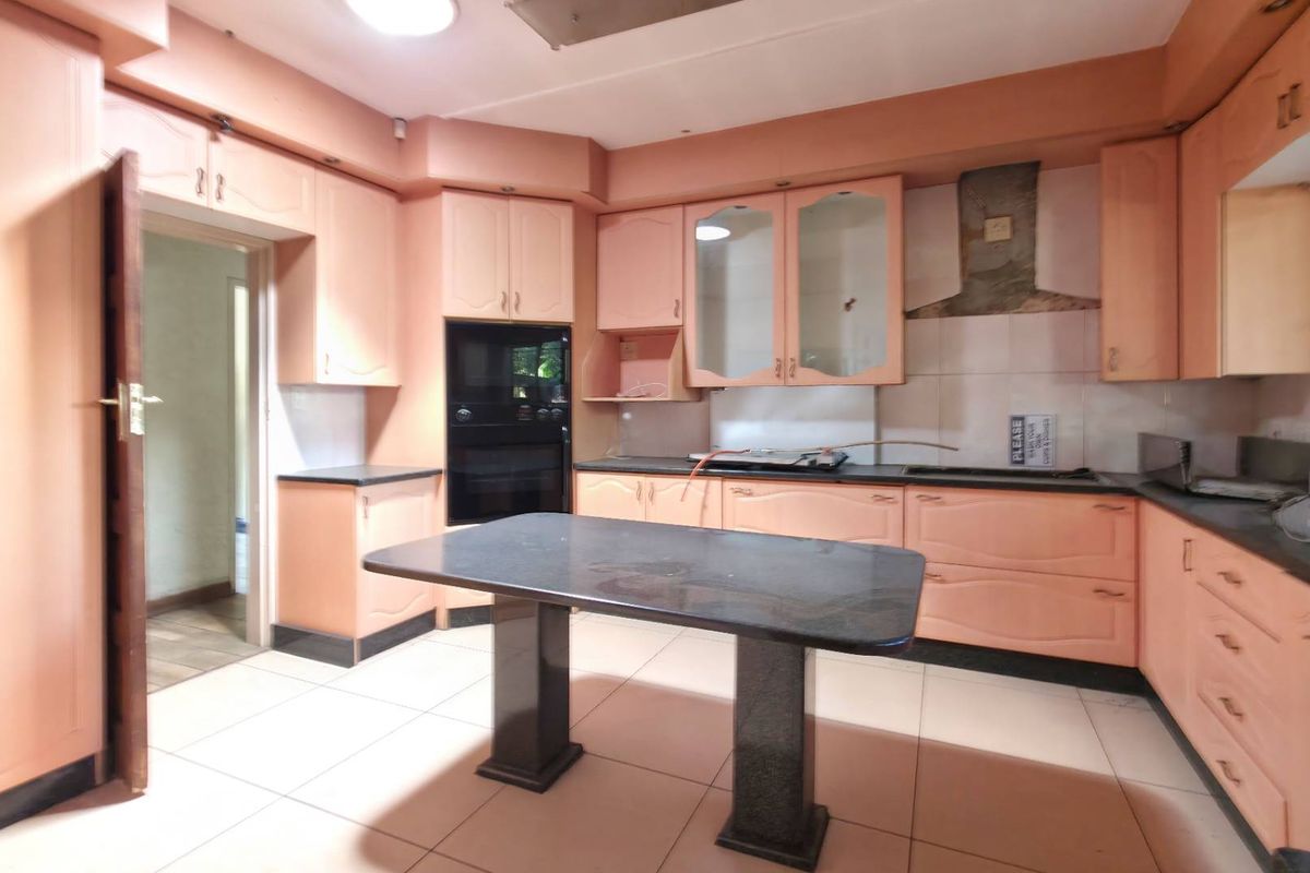 A dated kitchen featuring peach-toned cabinetry, a central stone-topped island, built-in oven, and tiled flooring, offering significant potential for a modern renovation.
