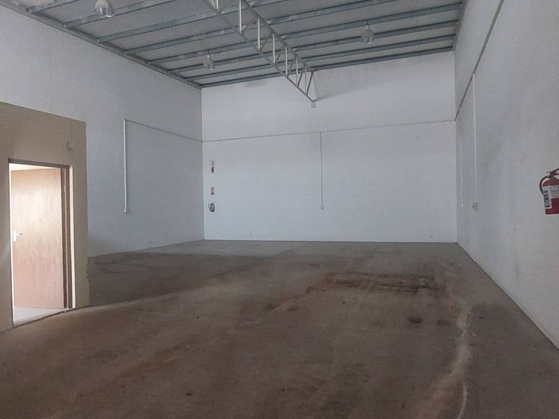 Spacious industrial warehouse unit featuring high ceilings with exposed steel trusses, concrete flooring, and an integrated internal office partition.
