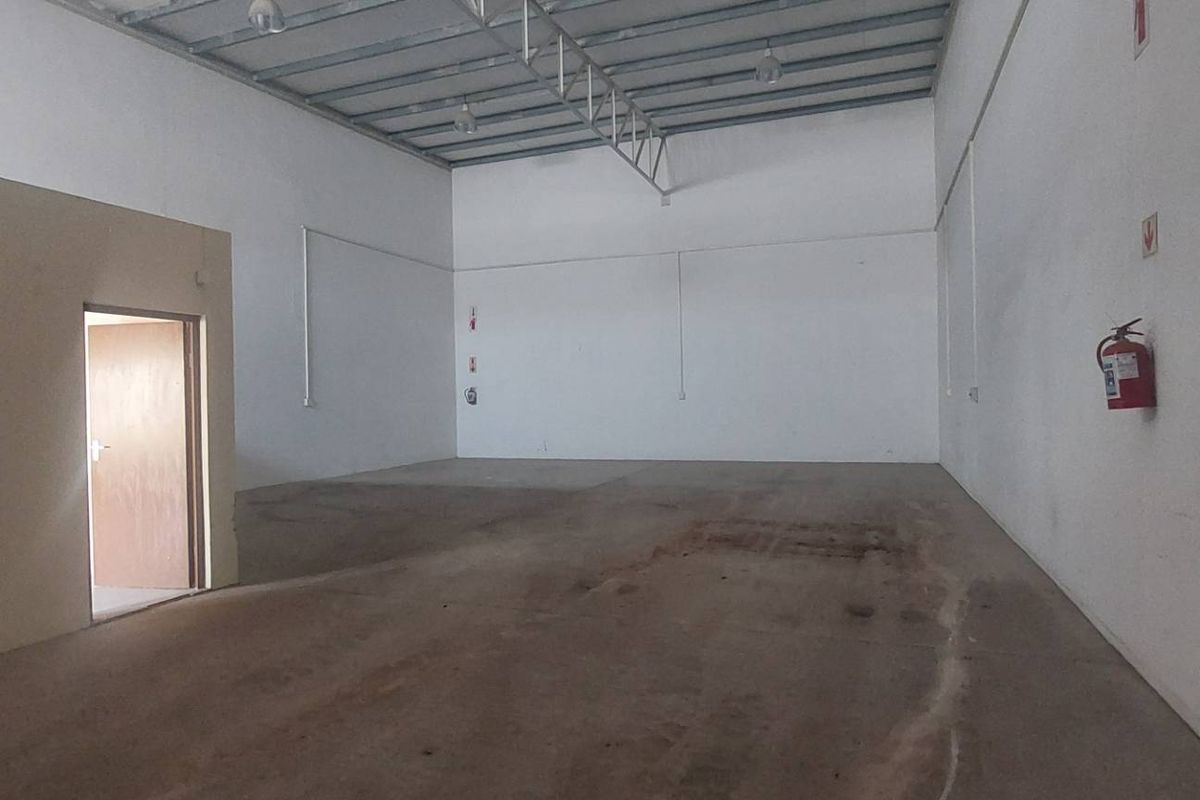 Spacious industrial warehouse unit featuring high ceilings with exposed steel trusses, concrete flooring, and an integrated internal office partition.