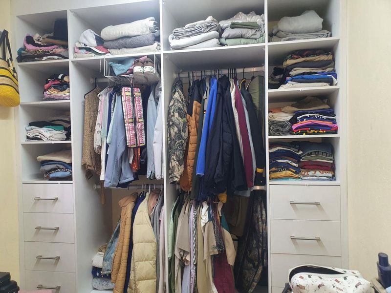 A functional built-in bedroom wardrobe featuring a combination of open shelving, hanging rails, and integrated storage drawers.