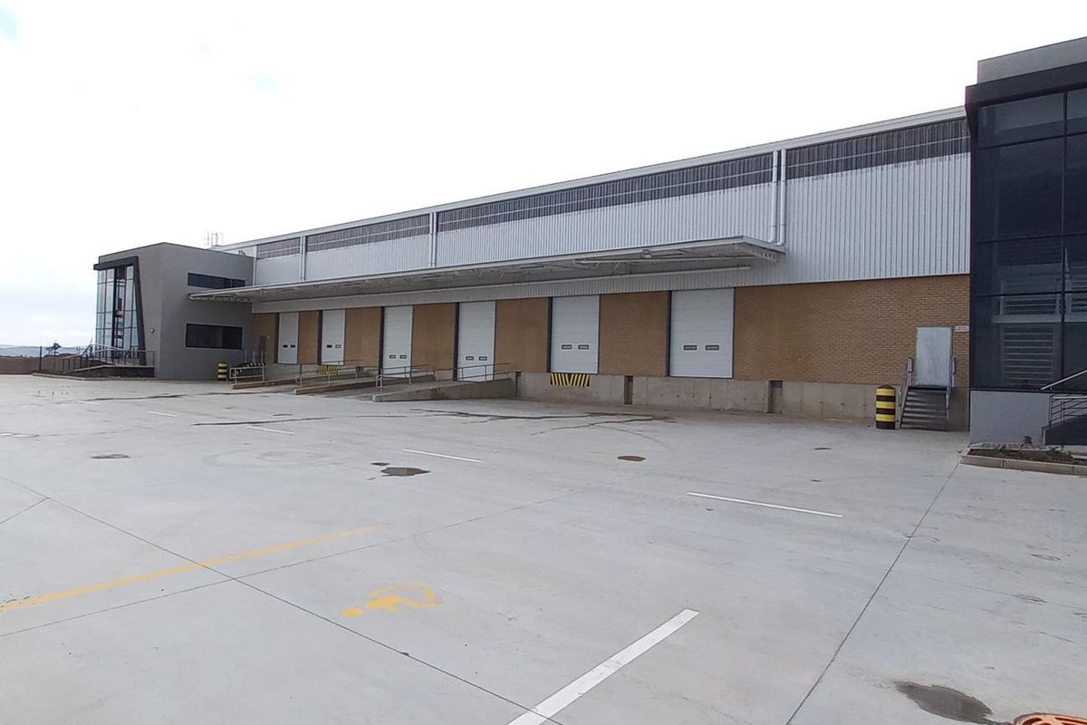 Modern industrial warehouse facility featuring multiple loading bays, concrete hardstand yard, and integrated office section with glass facade.