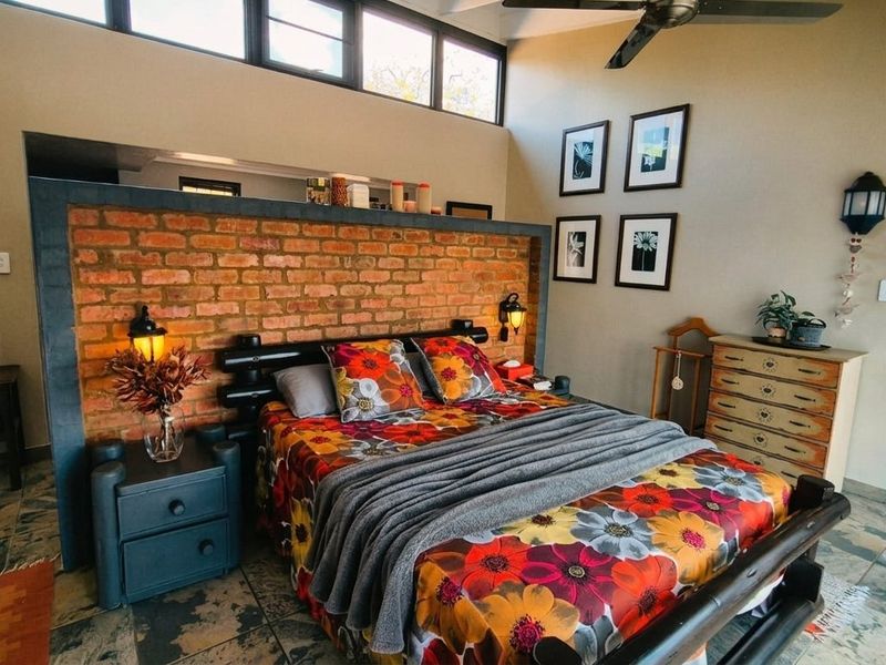 Spacious bedroom featuring an exposed brick feature wall, high ceilings with clerestory windows, a ceiling fan, and durable tiled flooring.
