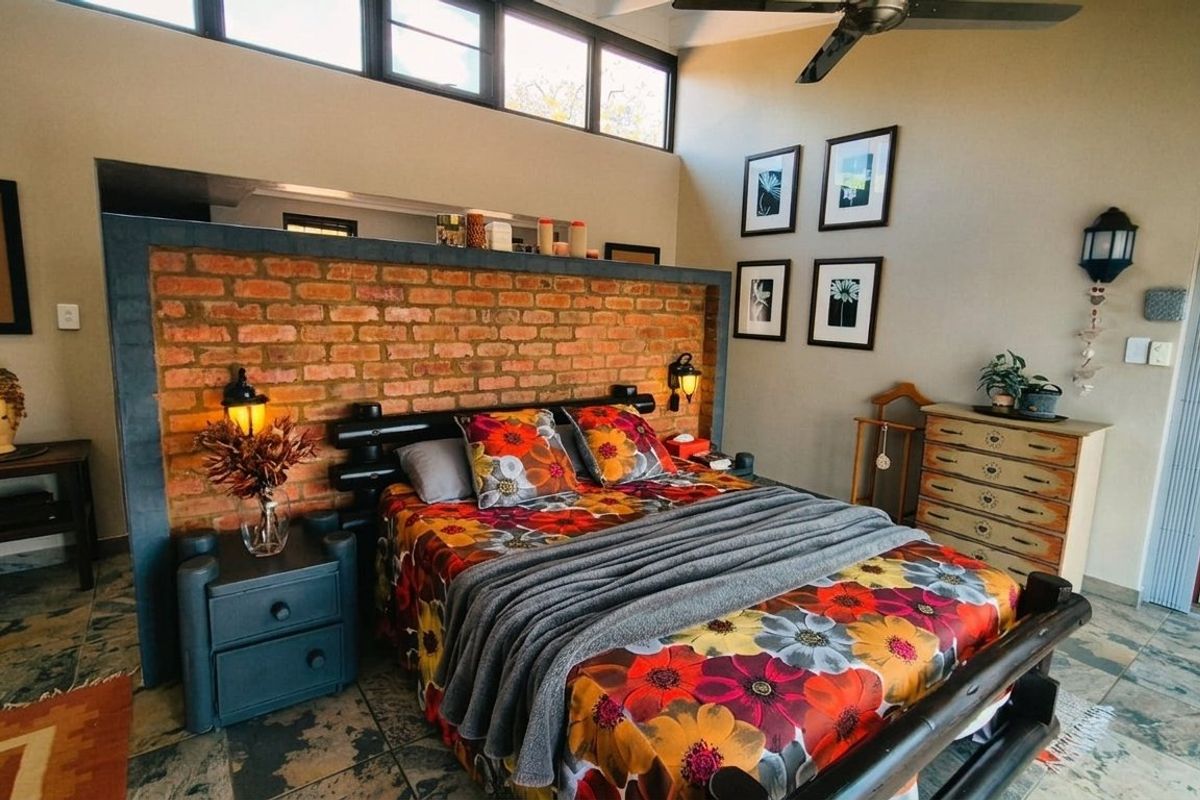 Spacious bedroom featuring an exposed brick feature wall, high ceilings with clerestory windows, a ceiling fan, and durable tiled flooring.