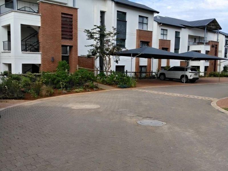Front view of a modern apartment complex featuring brick and white facade, paved driveway, and covered parking bays.