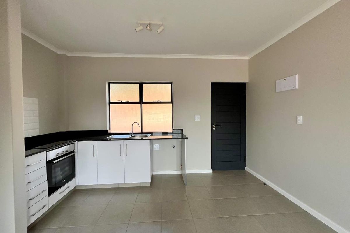 A clean, modern kitchen featuring white cabinetry, black granite countertops, built-in oven, and tiled flooring in an open-plan layout.