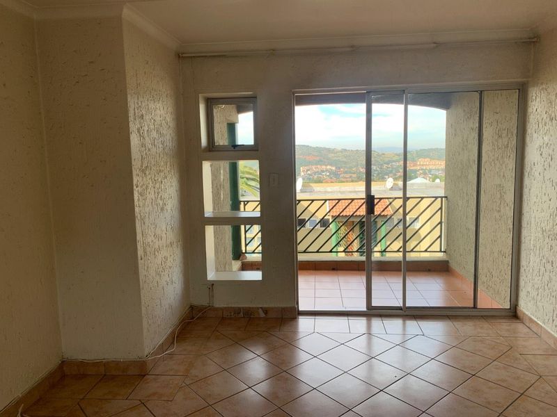 An empty living area featuring tiled flooring, textured walls, and a sliding glass door providing access to a balcony with scenic views.