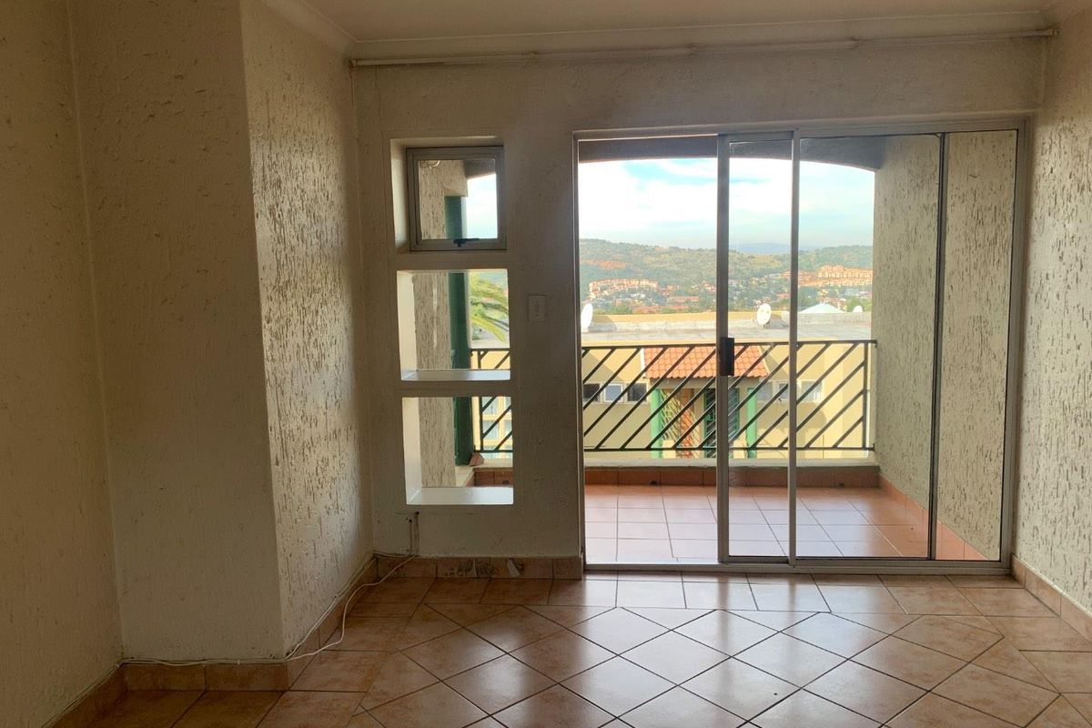 An empty living area featuring tiled flooring, textured walls, and a sliding glass door providing access to a balcony with scenic views.
