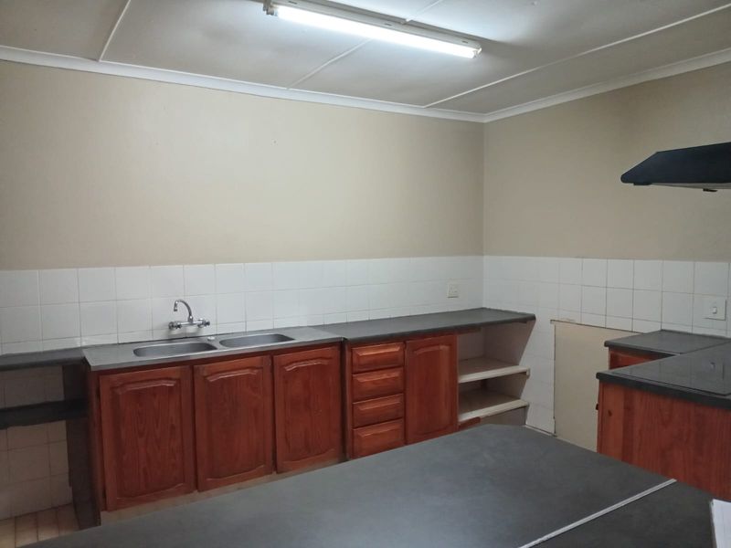 A functional kitchen space featuring wooden cabinetry, laminate countertops, a double sink, and a tiled backsplash, currently awaiting updates and finishing touches.