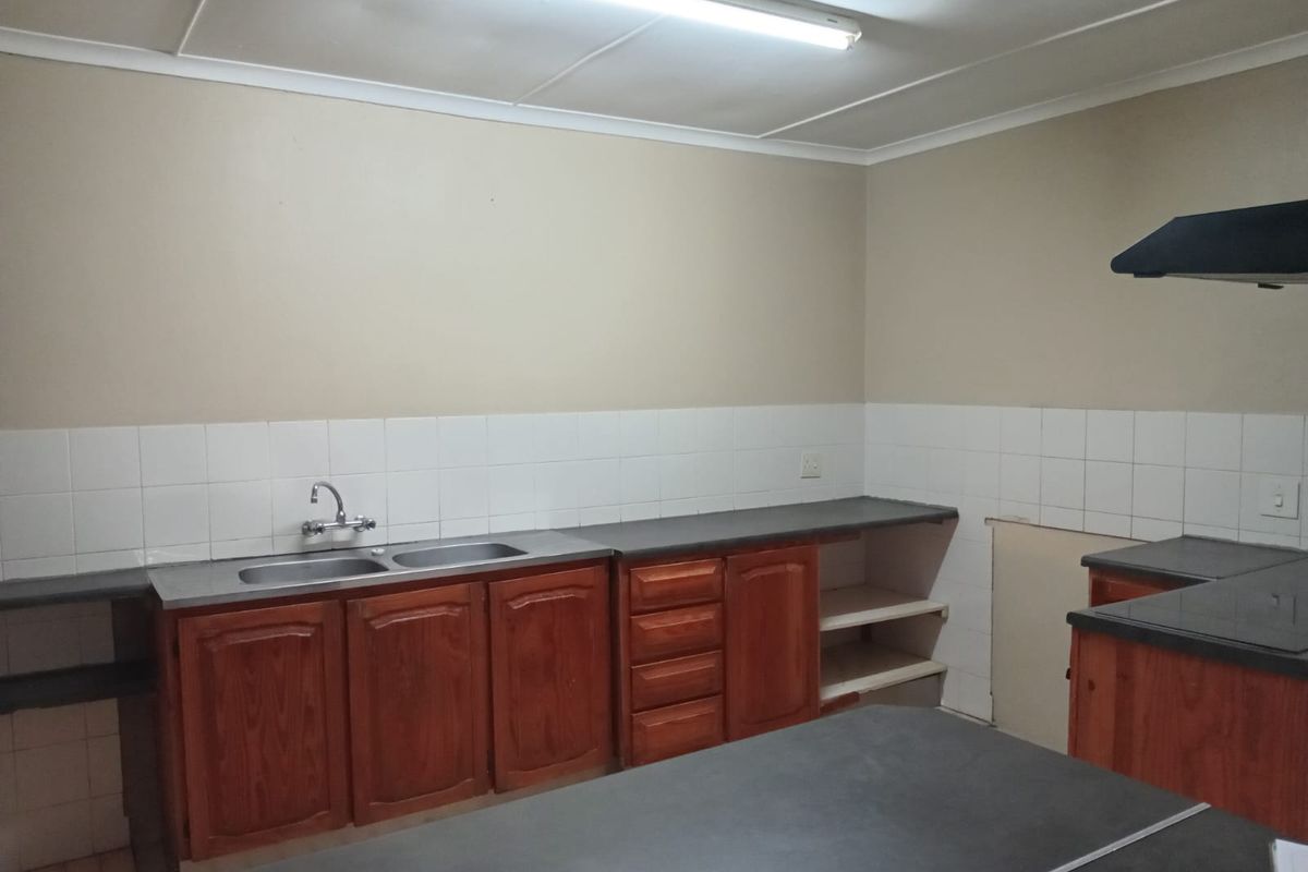 A functional kitchen space featuring wooden cabinetry, laminate countertops, a double sink, and a tiled backsplash, currently awaiting updates and finishing touches.