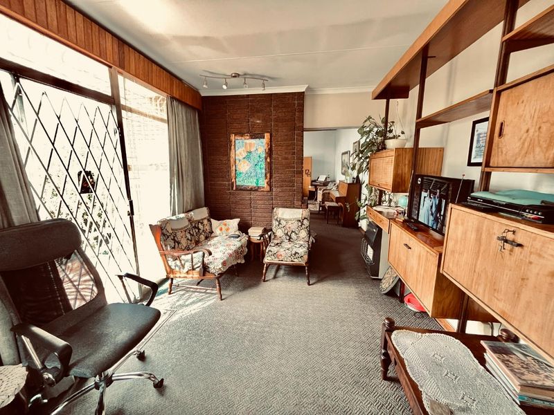 A living room featuring a brick accent wall, wood paneling, and large sliding glass doors with security gates, offering a dated but functional layout.