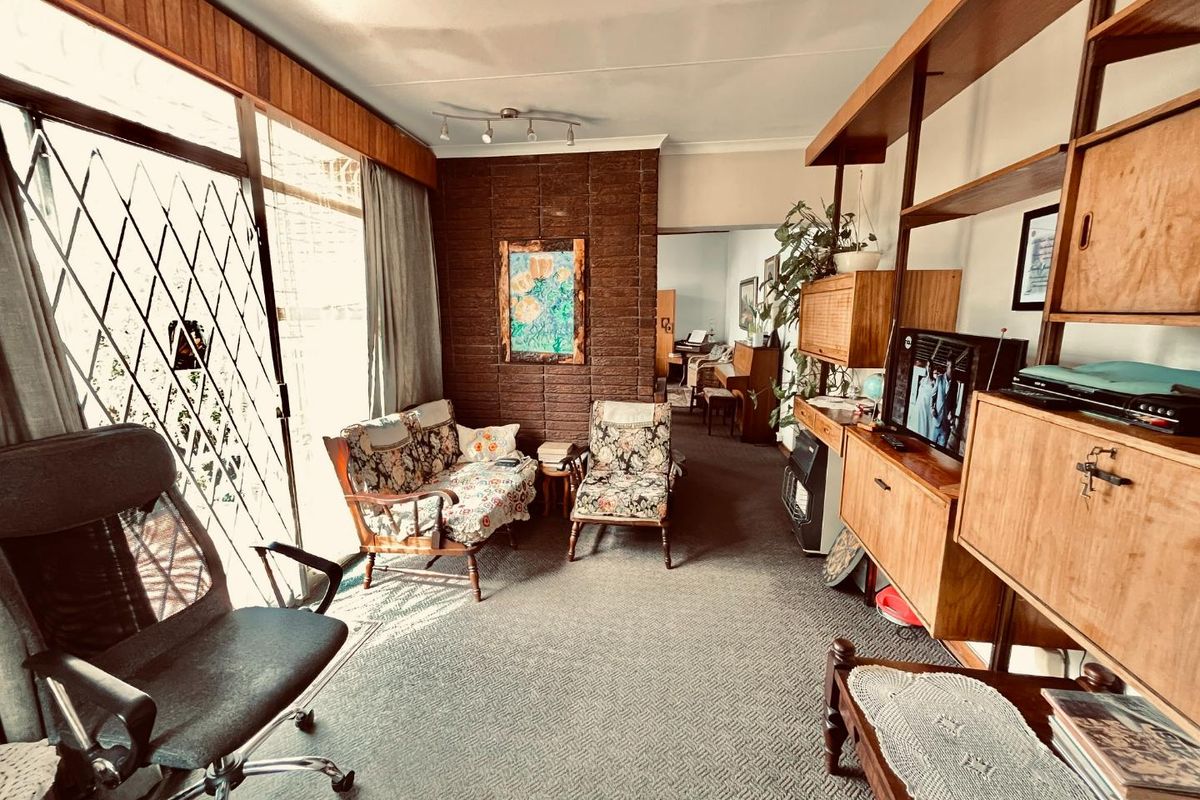 A living room featuring a brick accent wall, wood paneling, and large sliding glass doors with security gates, offering a dated but functional layout.