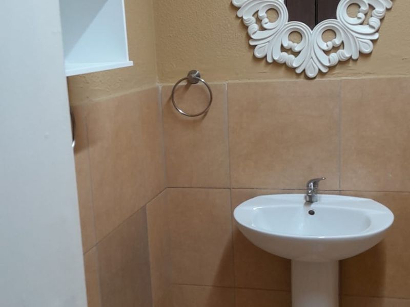 A compact bathroom featuring a white pedestal basin, tiled walls and flooring, and a wall-mounted storage cabinet.