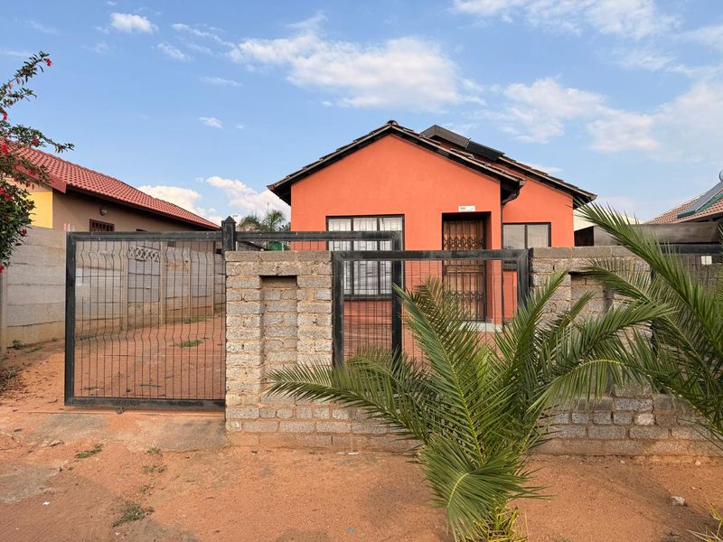 Front exterior view of a detached house featuring a perimeter wall, metal security gate, and a tiled roof with a solar geyser.