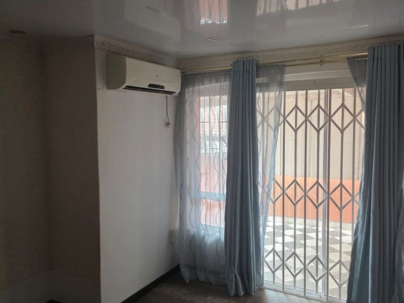 A bright living area featuring laminate flooring, a glossy ceiling, split-system air conditioning, and a sliding glass door with a security gate leading outside.