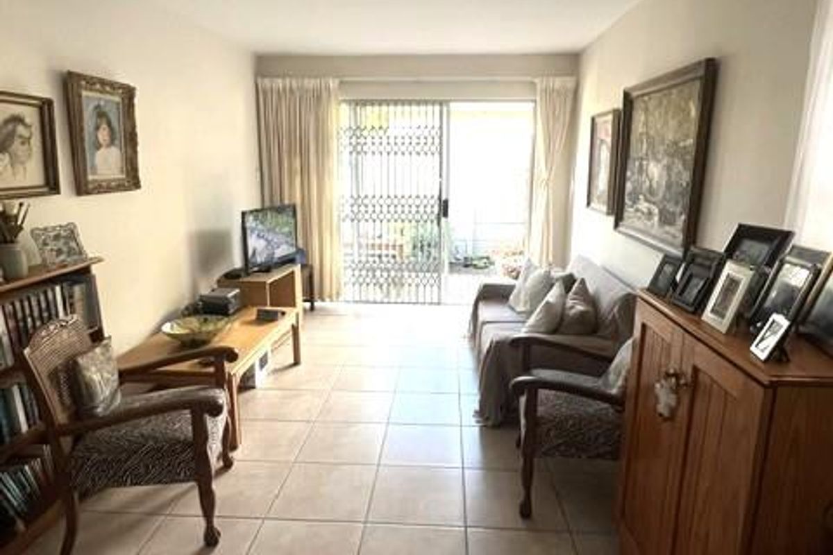 A living room featuring neutral tiled flooring and a sliding glass door with a security gate leading to an outdoor area.