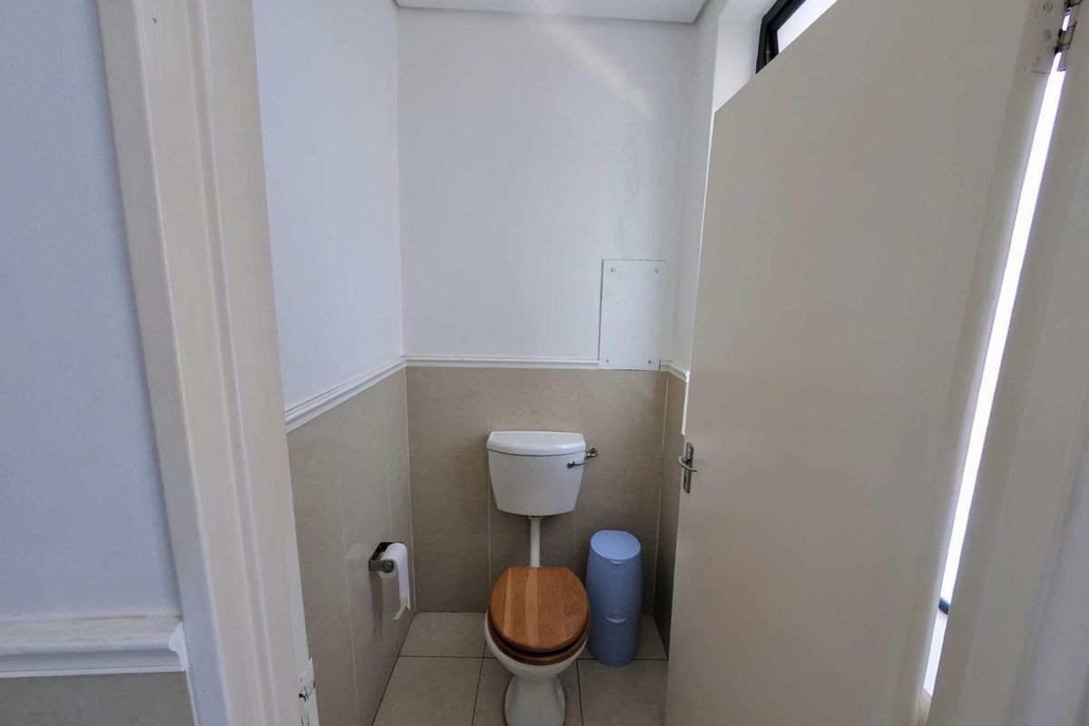 A compact office restroom featuring neutral wall tiling, a standard toilet, and a wooden seat.