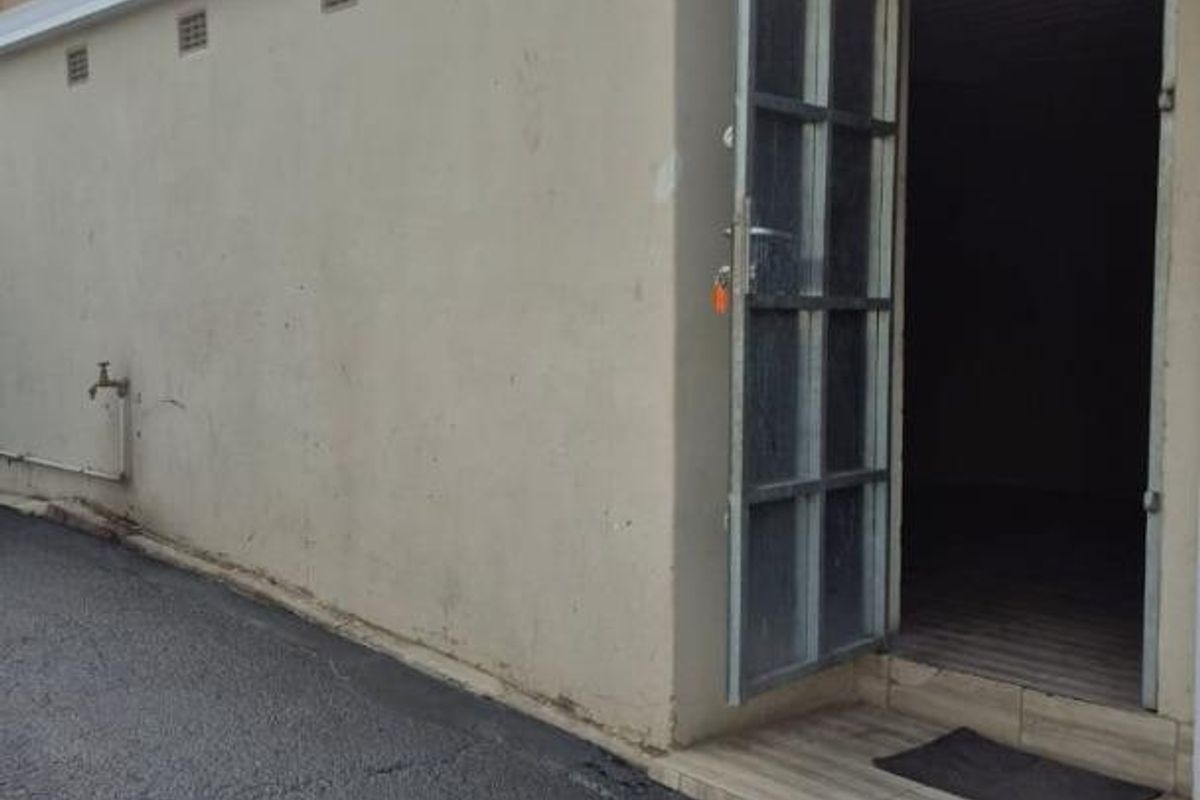 Exterior view of a rear building entrance featuring a metal security gate, tiled step, and external water tap access.