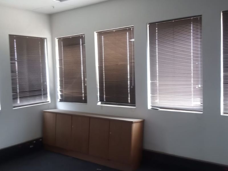 An empty office space featuring multiple windows with venetian blinds and built-in low-level cabinetry along the wall.