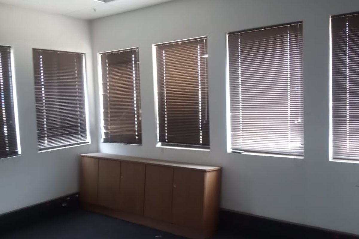 An empty office space featuring multiple windows with venetian blinds and built-in low-level cabinetry along the wall.