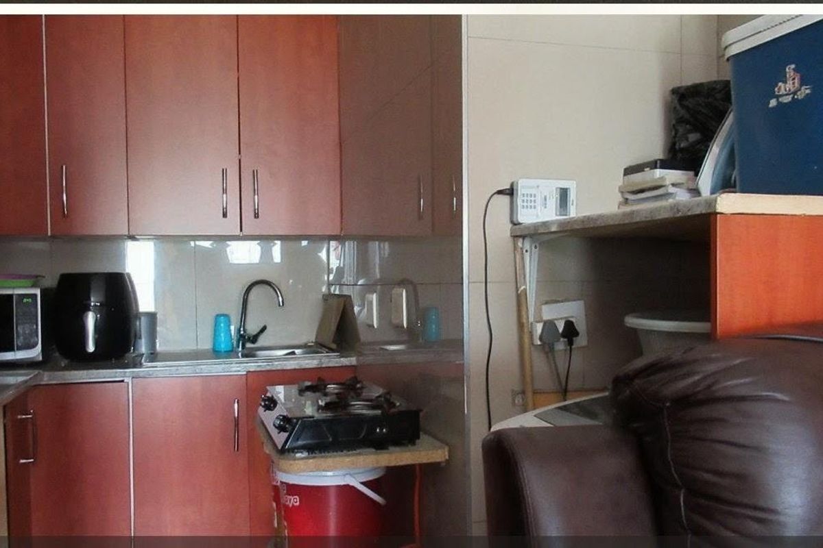 A compact kitchen featuring wood-look laminate cabinetry, a stainless steel sink, and tiled backsplash, requiring modernization to improve functionality and aesthetic appeal.