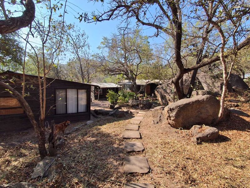 A rustic exterior view of the property featuring timber-clad structures set within a natural landscape with stone pathways and large boulders.
