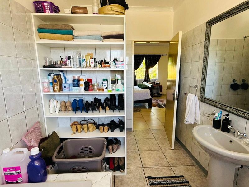 A functional bathroom featuring tiled walls and flooring, a pedestal basin, a large wall mirror, and a built-in storage shelving unit.