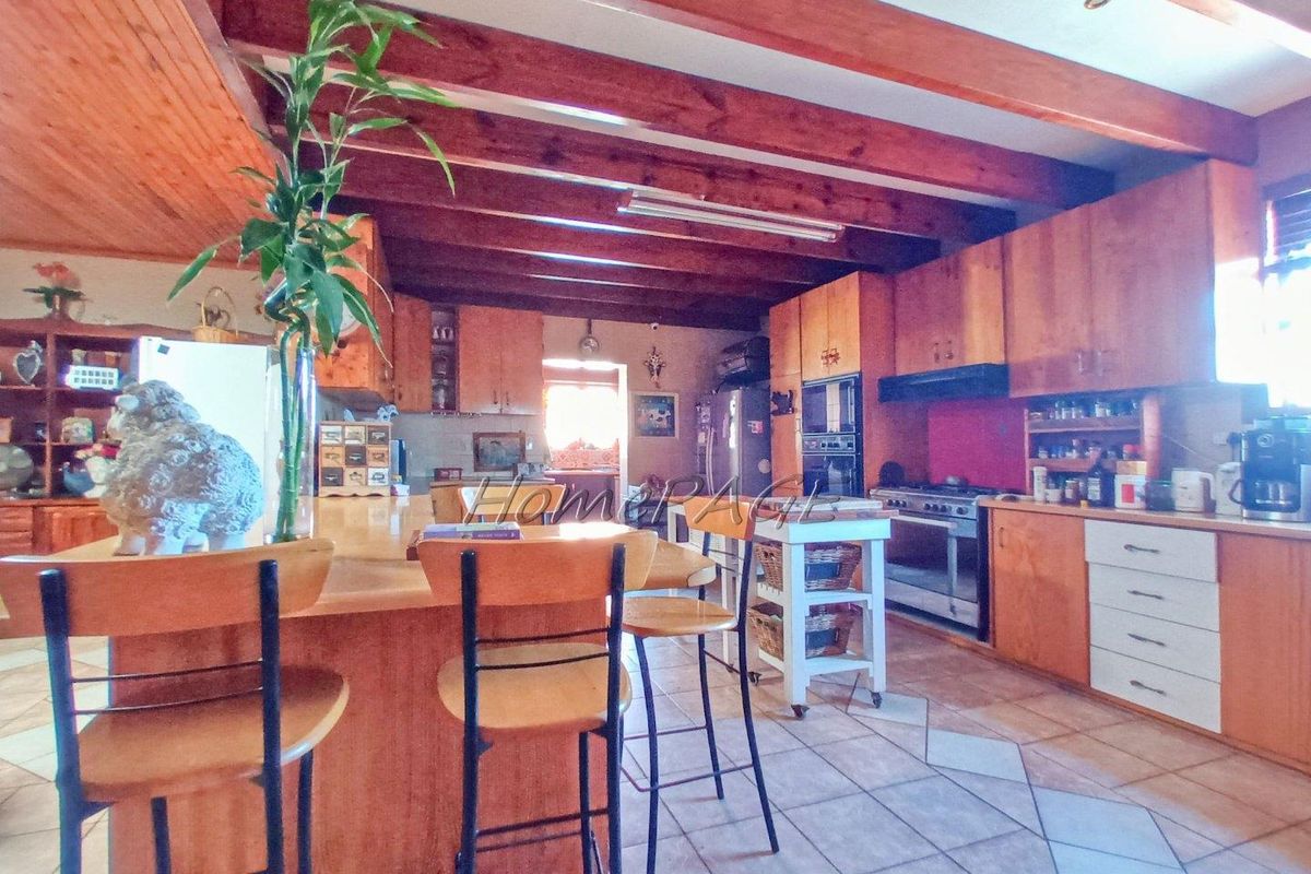 Spacious kitchen featuring timber cabinetry, exposed wooden ceiling beams, a central breakfast island, and integrated oven and hob.