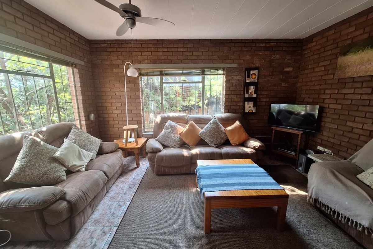 A cozy living room featuring exposed brick walls, large windows with security bars, and a ceiling fan, creating a rustic and comfortable atmosphere.