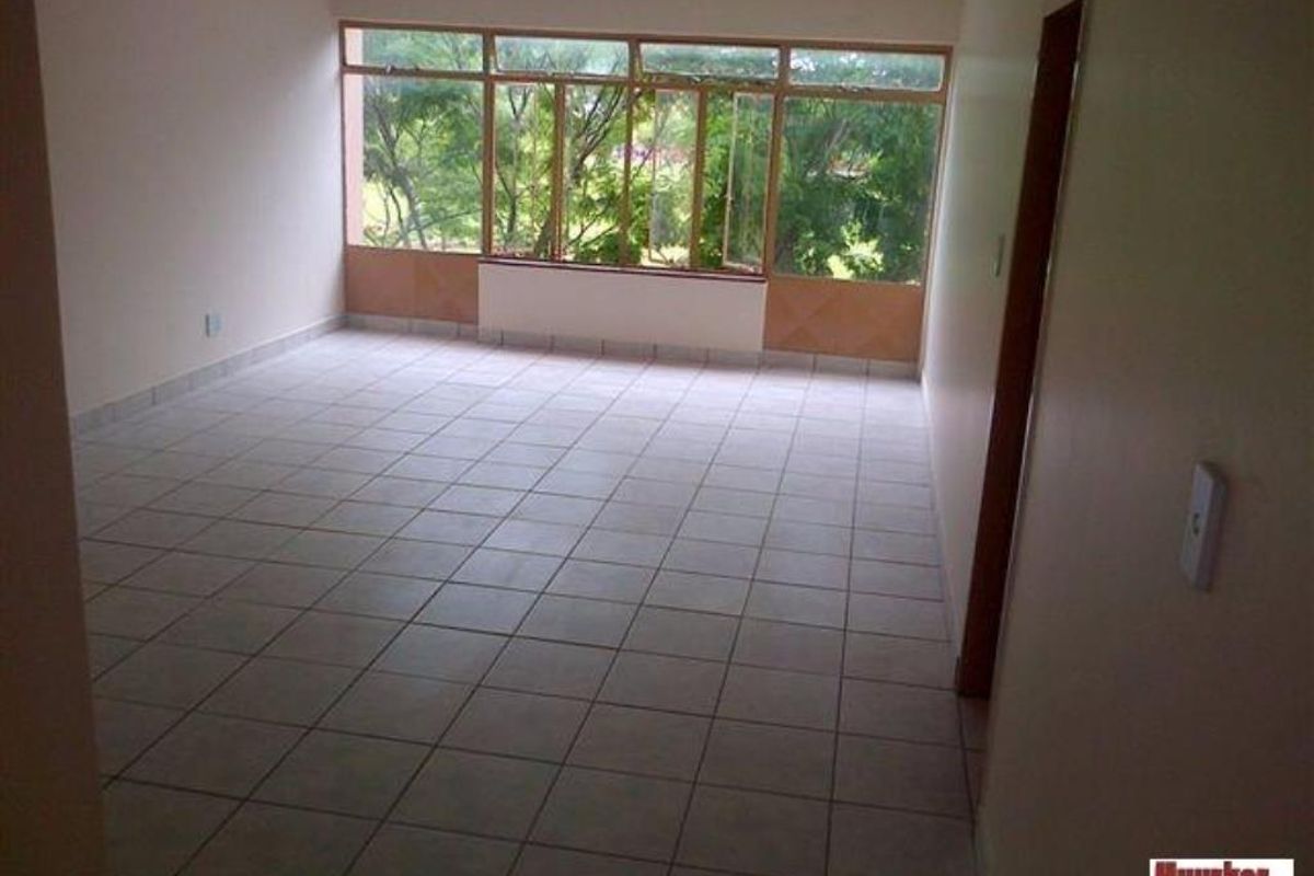 An empty living room featuring neutral tiled flooring and large windows that provide natural light and a view of the surrounding greenery.