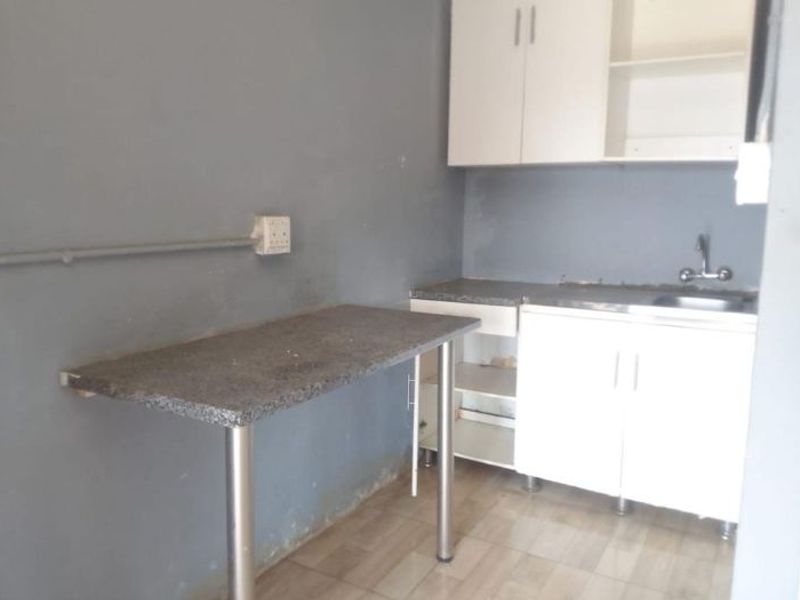 A compact kitchen area featuring basic built-in cabinetry, a stainless steel sink, and a small breakfast bar, requiring cosmetic updates and finishing touches.