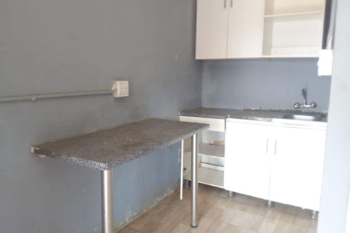 A compact kitchen area featuring basic built-in cabinetry, a stainless steel sink, and a small breakfast bar, requiring cosmetic updates and finishing touches.