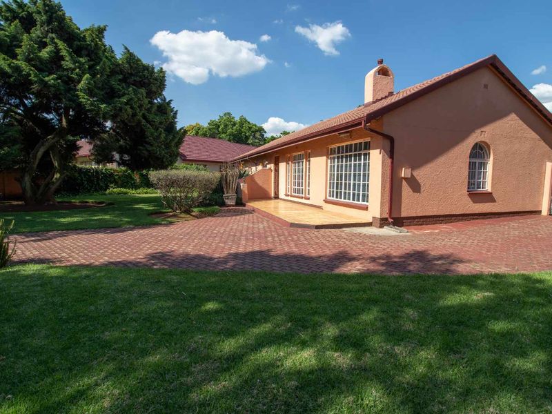 A well-maintained single-story house featuring a tiled roof, brick-paved driveway, and a covered patio area set within a landscaped garden.