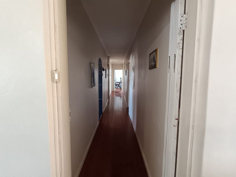 A long, narrow hallway featuring polished hardwood flooring and neutral wall finishes, providing access to various rooms within the home.