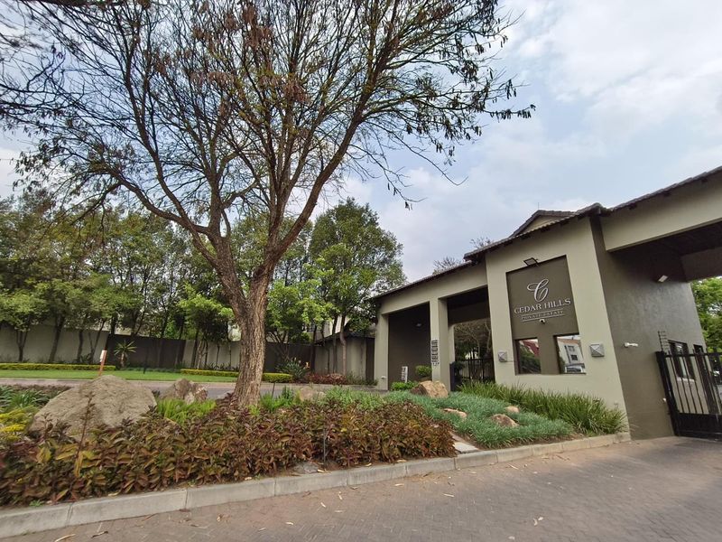 The entrance to Cedar Hills Private Estate, featuring a secure gatehouse, paved driveway, and well-maintained landscaped gardens.