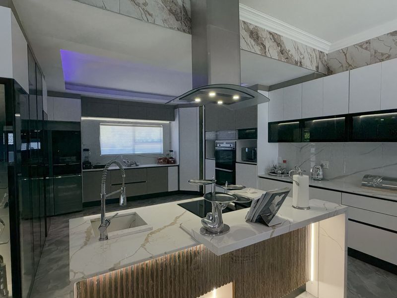 Modern, high-end kitchen featuring a central island with stone countertops, integrated appliances, sleek cabinetry, and sophisticated LED accent lighting.