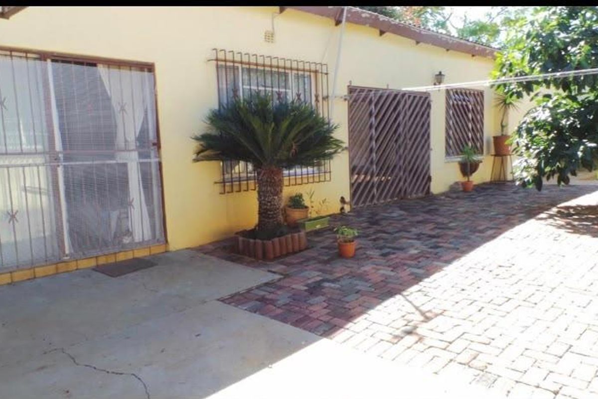 Rear exterior view of the property featuring a paved patio area, security bars on windows, and sliding door access.