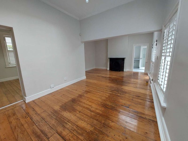 Spacious living area featuring original hardwood flooring, a classic fireplace, and plantation shutters, offering a bright and neutral canvas for interior design.