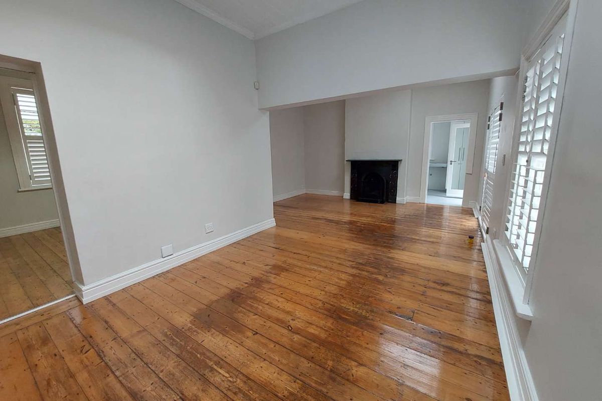 Spacious living area featuring original hardwood flooring, a classic fireplace, and plantation shutters, offering a bright and neutral canvas for interior design.