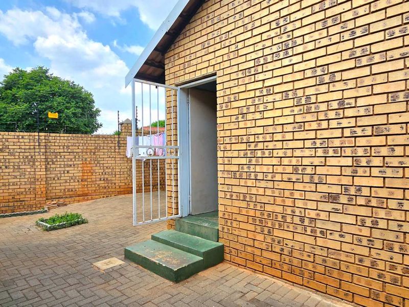 A private rear courtyard featuring face brick walls, paved flooring, and secure access with a metal gate and concrete steps.